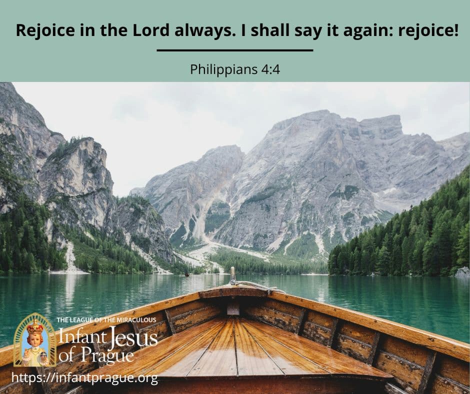Front of wooden boat with mountains, trees, and calm water ahead.